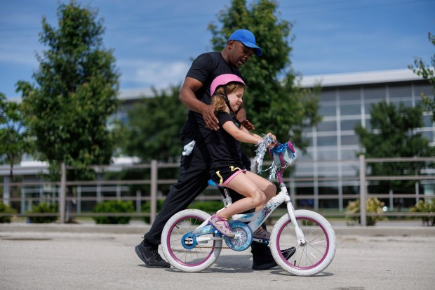Louie Burrel, 45, teaches Alex White, 6, how to ride a bike in a parking lot in the Morgan Park neighborhood on June 2, 2024, in Chicago.  (Armando L. Sanchez/Chicago Tribune)